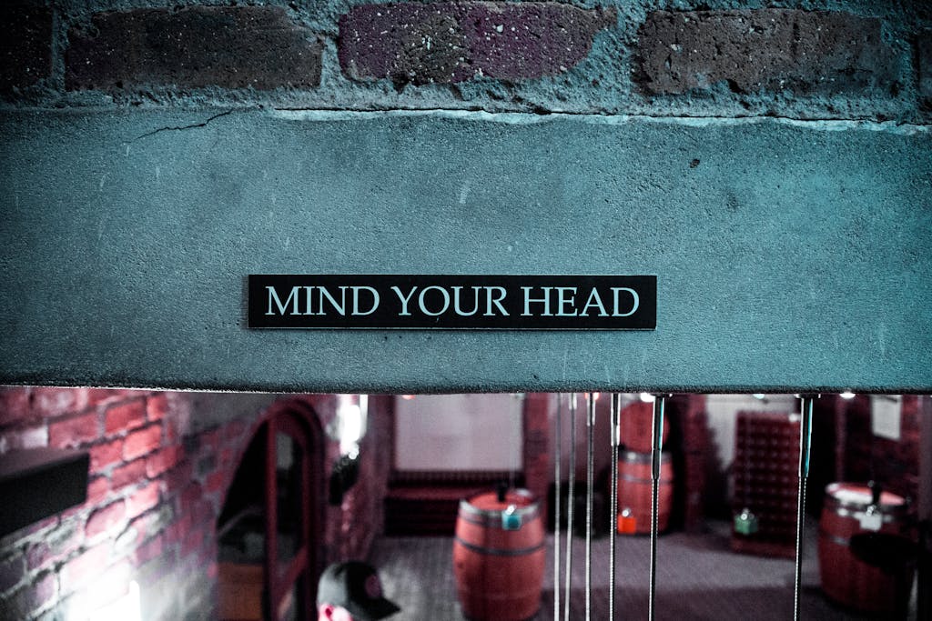 A 'Mind Your Head' sign in a rustic brick barrel cellar setting, creating a safety awareness ambiance.