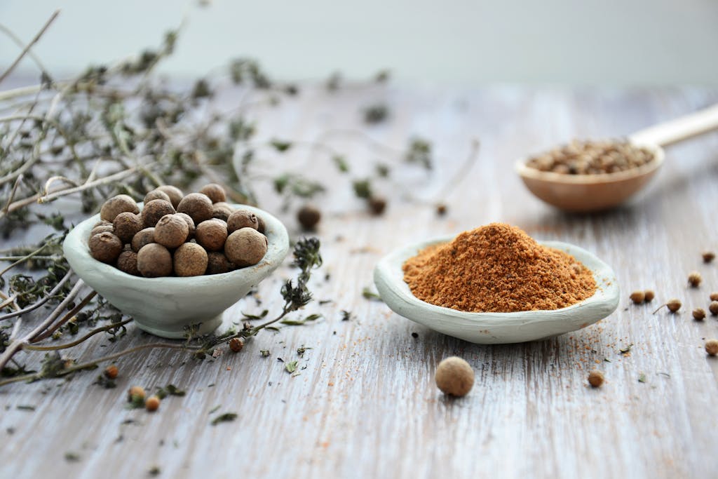 An artistic display of whole and ground spices in ceramic bowls on a rustic wooden surface, emphasizing culinary tradition.